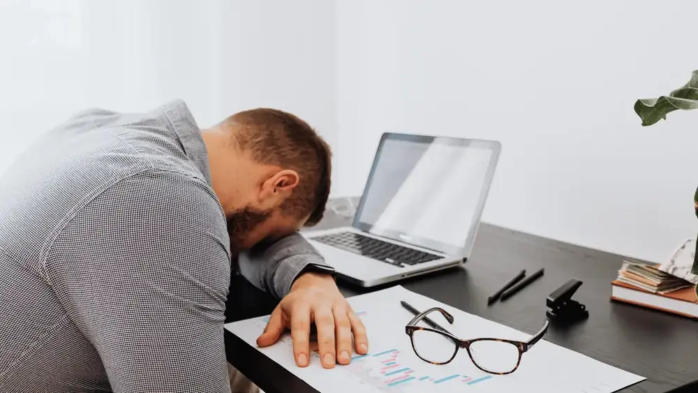 Homem cansado, com a cabeça apoiada na mesa do escritório